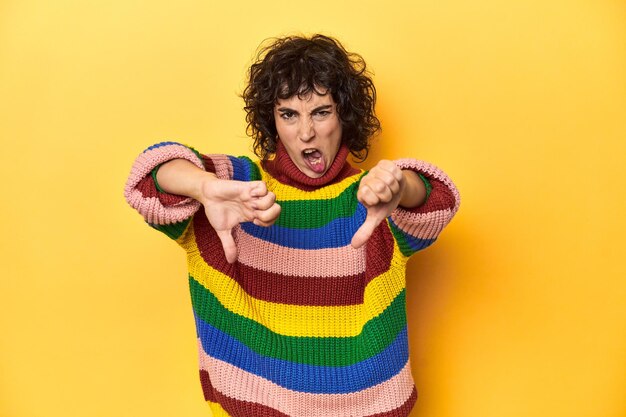 Curlyhaired woman in multicolor sweatshirt showing thumb down and expressing dislike