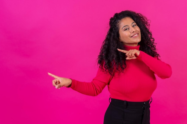 Curlyhaired donna che punta a sinistra su uno sfondo rosa girato in studio copia incolla