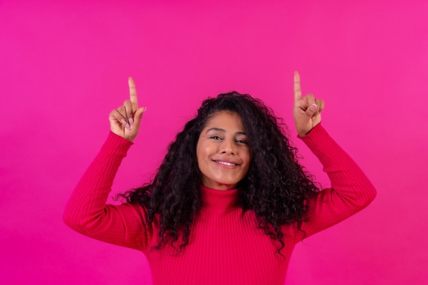 Curlyhaired donna che punta verso l'alto su uno sfondo rosa girato in studio copia incolla