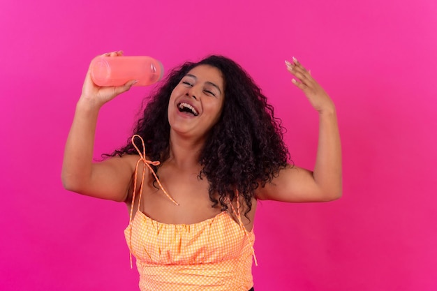 Donna dai capelli ricci in abiti estivi su uno sfondo rosa che beve acqua riscaldata girato in studio