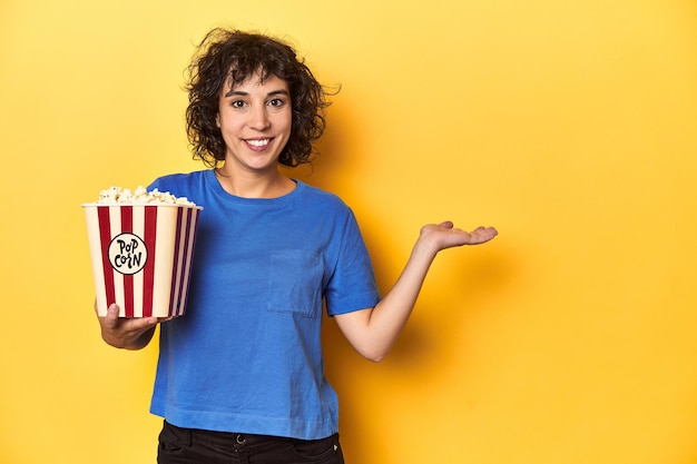 パームのコピースペースを示す映画スタジオ用のポップコーンを持ったカーリヘアの女性