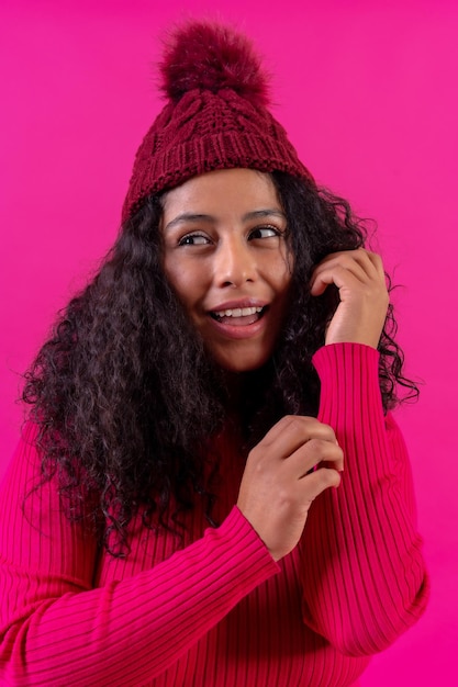 Curlyhaired woman in a wool cap on a pink background portrait smiling studio shot