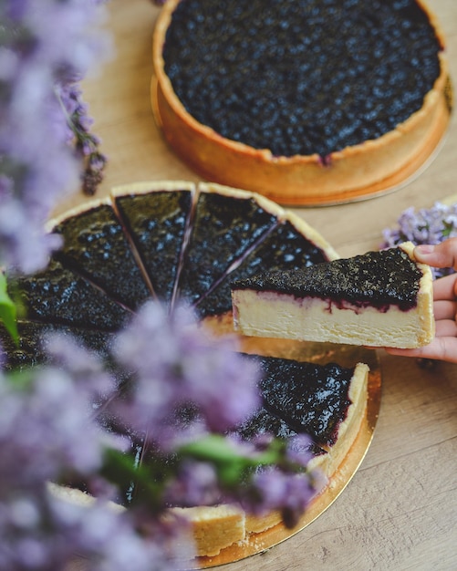 currant cheesecake on a wooden table with lilac bush around, child's hand holding a piece of cake