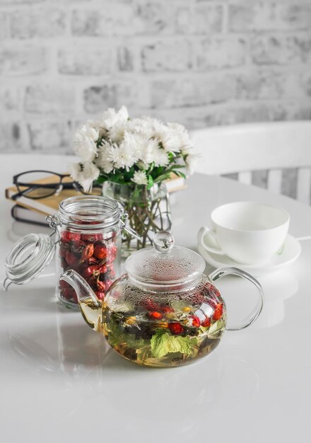 Currant raspberry leaves rose hips herbal tea in glass teapot on kitchen table Rising immunity Home cozy still life