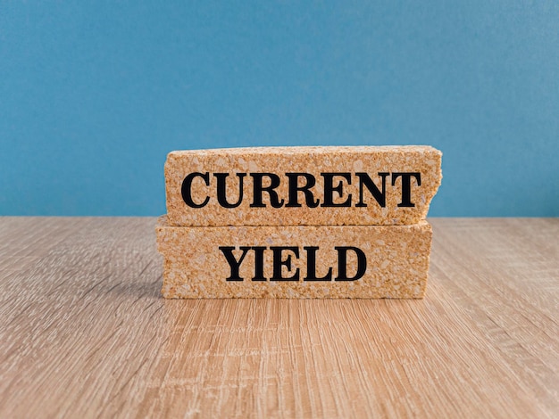 Current Yield text concept on brick blocks Beautiful wooden table blue background Copy space