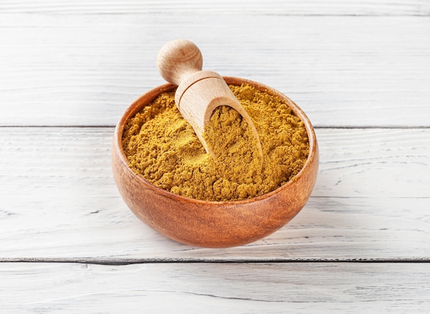 Photo curry powder in wooden bowl with scoop on white wooden background