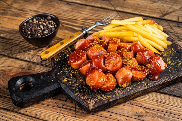 Curry wurst Sausages with French fries on a wooden board