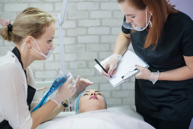Cursus permanente make-up. Schoonheidsspecialiste die vrouwelijke stagiaire leert hoe ze symmetrische wenkbrauwen moet schetsen.