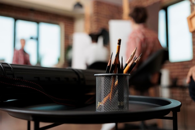 Cursus schetsen. Close up van metalen standhouder met grafietpotloden staande op tafel tegen een groep mensen studenten zitten op ezels op onscherpe achtergrond, studeren tekenen in kunstatelier