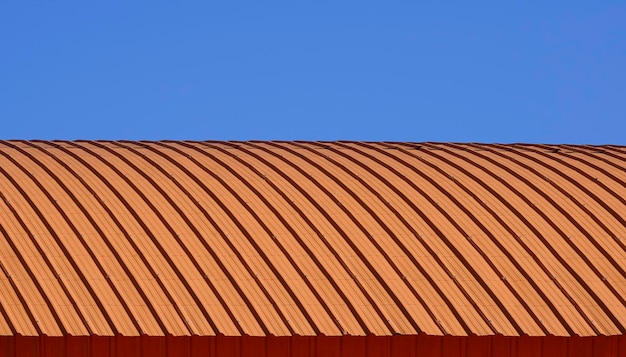 Фото Изогнутая крыша из оранжевой гофрированной стали на фоне голубого ясного неба