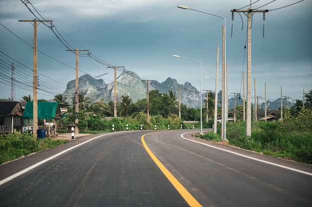 Curved asphalt road with mountain range and utility pole and lamppost in countryside at Sam Roi Yot, Prachuap Khiri Khan