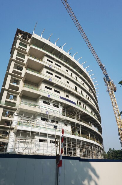 Curved building construcion facade in progress with tall crane against blue sky