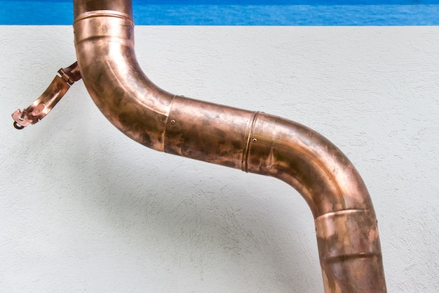 Curved copper pipe outside the building for water draining on the background of white plaster wall