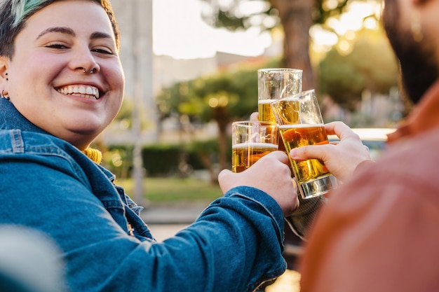 お祝いのトーストのための短い髪のチャリンというビールグラスと曲線美の非バイナリ