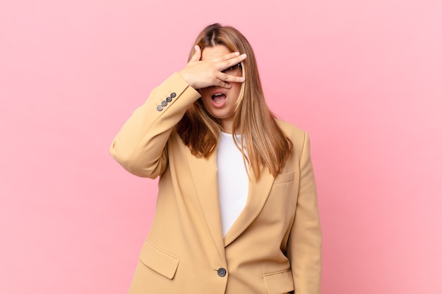 Curvy pretty blonde woman looking shocked, scared or terrified, covering face with hand