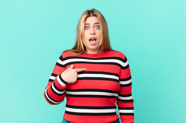 Curvy pretty blonde woman looking shocked and surprised with mouth wide open, pointing to self