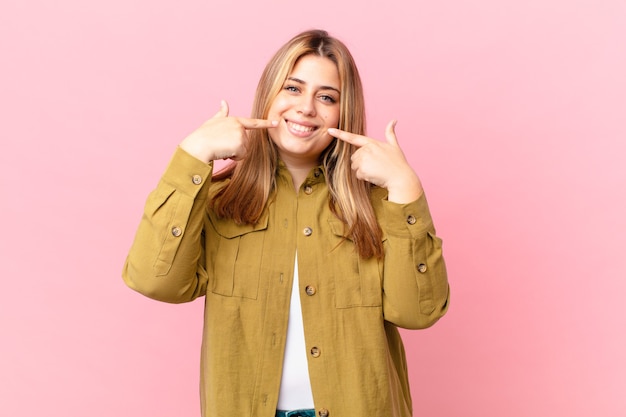 Curvy pretty blonde woman smiling confidently pointing to own broad smile