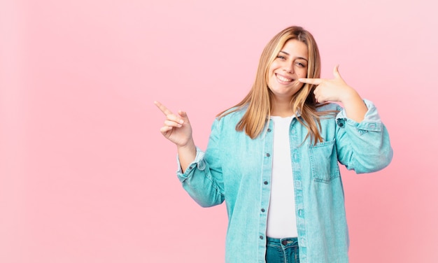 Curvy pretty blonde woman smiling confidently pointing to own broad smile