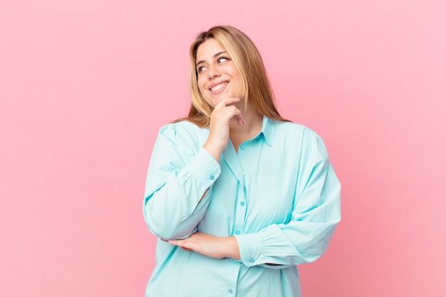 Curvy pretty blonde woman smiling with a happy, confident expression with hand on chin