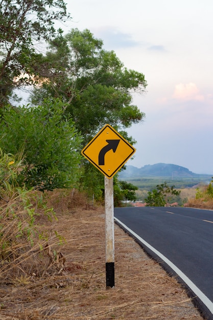 Photo curvy road sign beside country road