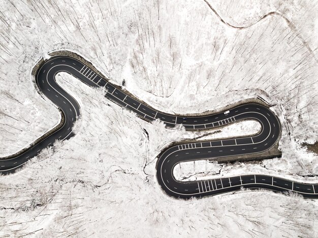 Foto strada curva e ventosa nella foresta coperta di neve, vista aerea dall'alto verso il basso