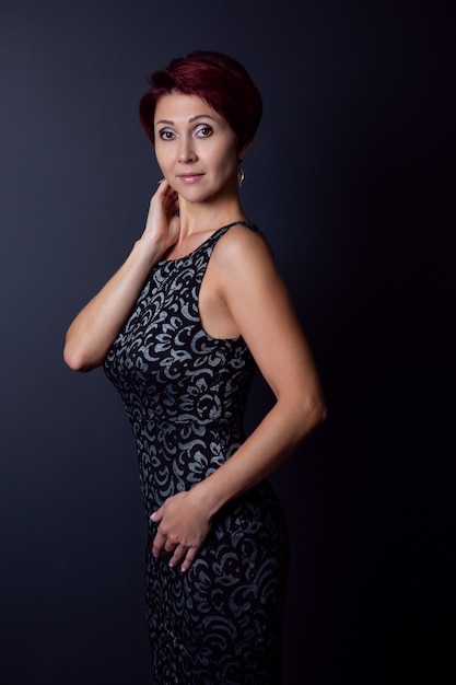 A curvy woman in a black dress poses on a dark background