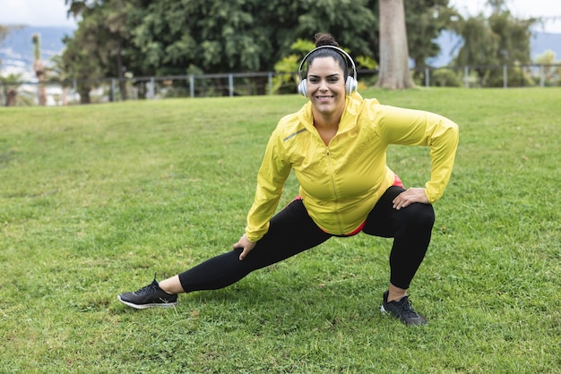 Curvy woman doing stretching day routine outdoor at city park - Plus size and workout sport exercises concept - Focus on face