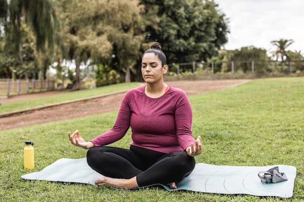 Photo curvy woman doing yoga meditation outdoor at city park - focus on face