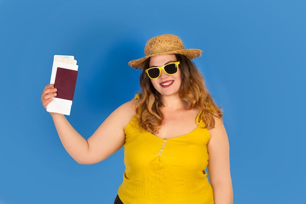 Curvy woman holding passport and plane tickets on a blue