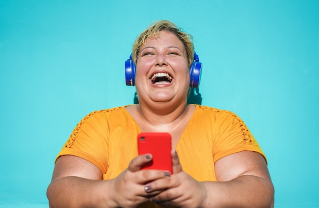매력적인 여자 웃음과 스마트 폰 야외 사용-휴대 전화에 재미 듣는 음악 재생 목록을 가진 젊은 여성
