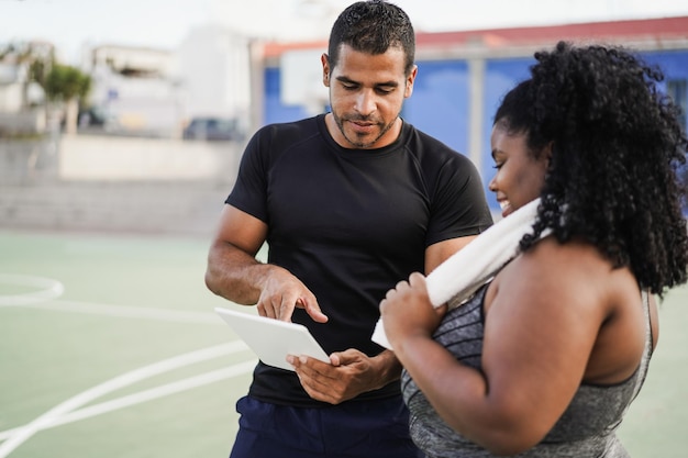 Foto donna formosa che parla con il suo personal trainer mentre controlla gli appunti tecnologici all'aperto focus sul trainer