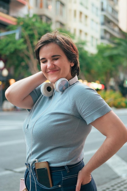 Curvy woman with short hair and headphones looks at the camera and smiles on a city street