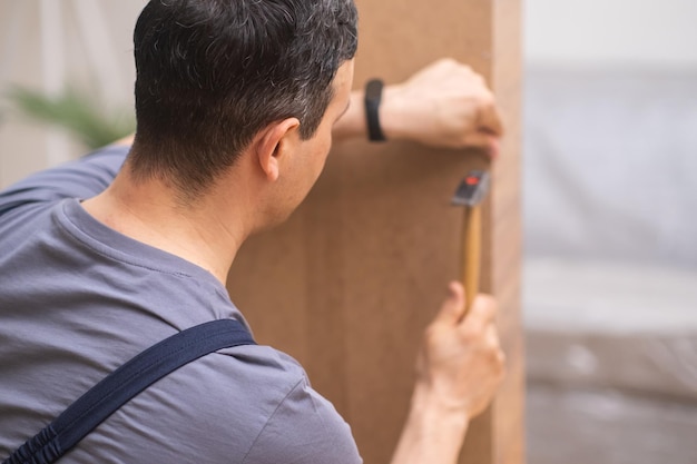 Custom furniture production focused worker hammering nail into wardrobe made of wood