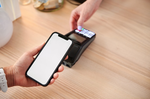 A customer in a cafe makes a contactless payment using an online application on his phone. Close-up of owner and customer accounting with contactless payment. Non contact payment concepts