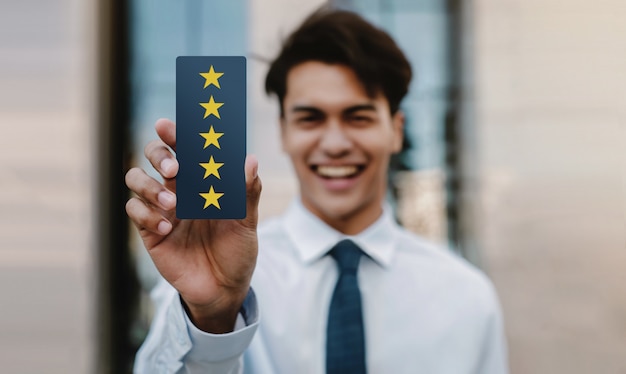 Концепция клиентского опыта. Счастливый молодой бизнесмен дает пять звезд рейтинга и положительный отзыв на карте. Опросы удовлетворенности клиентов. Передний план