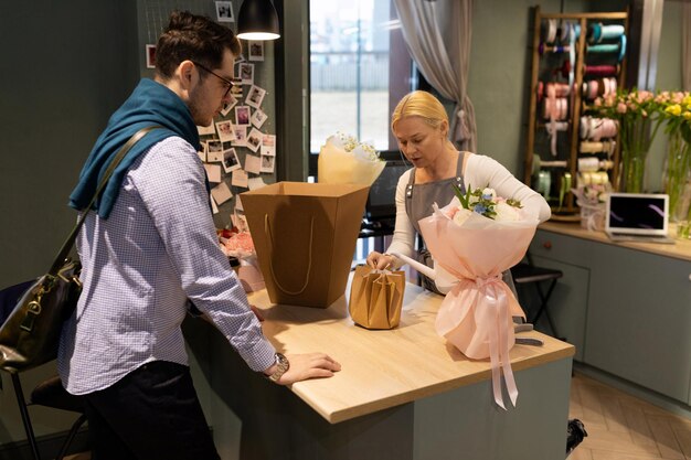 A customer in a flower shop picks up a fresh bouquet prepared by a florist and wrapped in gift paper