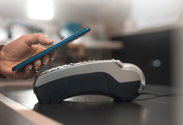 Customer hand pays with smartphone in store using NFC technology. Mobile phone paying the bill with contact less technology.