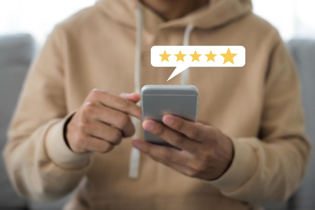 Foto mano del cliente che preme sullo schermo dello smartphone con l'icona del feedback di valutazione a cinque stelle e il livello di stampa eccellente per dare il miglior punteggio per rivedere il servizio clienti