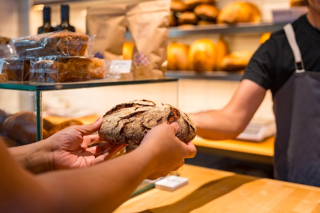 Customer hands in the bakery shop buying an artisan bread from the baker in the workshop workshop