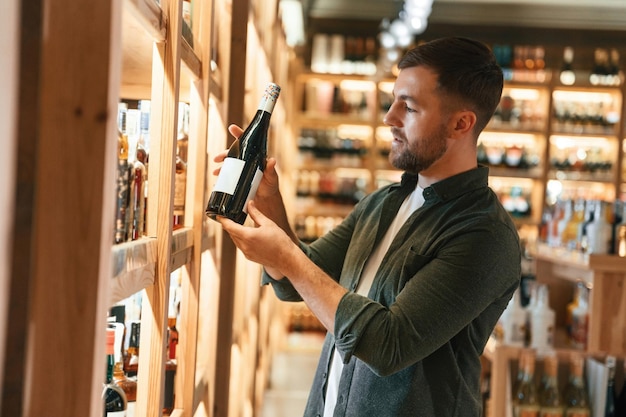 Foto il cliente sta guardando la bottiglia l'uomo sta scegliendo il vino nel negozio