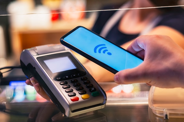 Customer is paying with smartphone in shop using NFC technology. against the background of the payment terminal and the seller's girl.