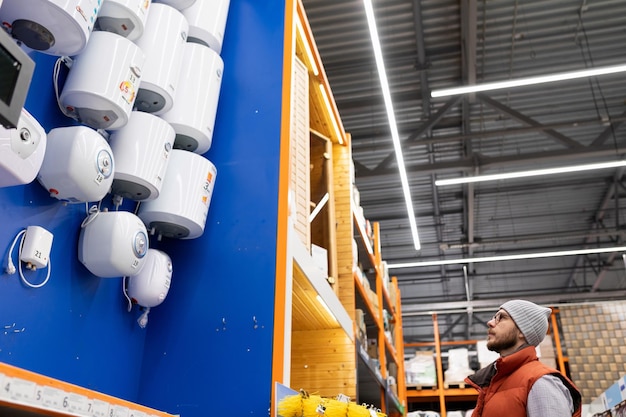 A customer in a plumbing hypermarket chooses a new hot water boiler for his home