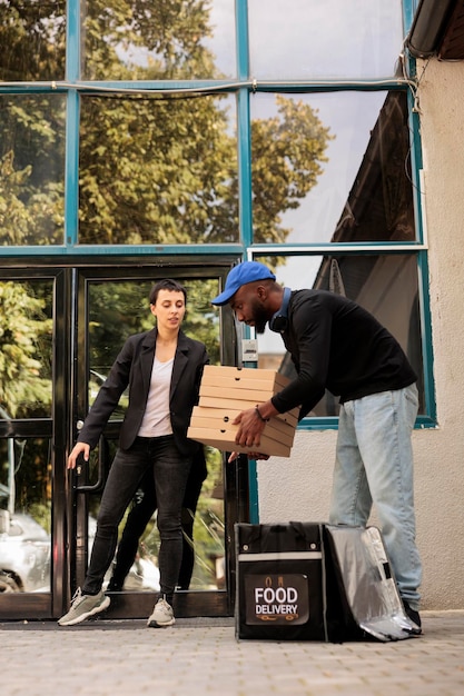 Customer receiving pizza boxes pile, courier taking out order from thermal backpack outdoors. Food delivery service, pizzeria african american deliveryman holding takeaway lunch