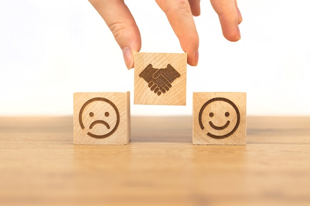 Customer satisfaction concept. Smiley and sad face icon on a wooden cube, hand shaking. Service rating, review or survey, marketing business background photo