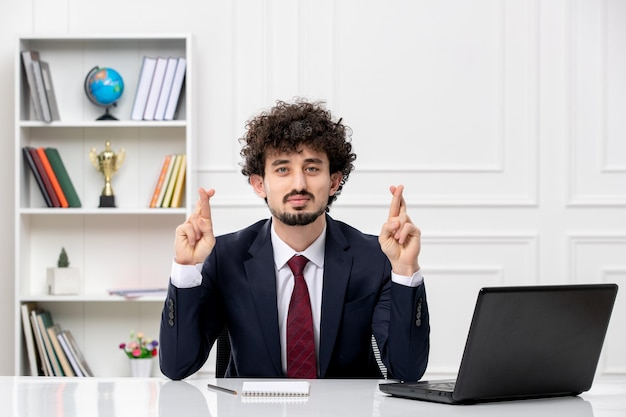 Customer service curly brunette young man in office suit and red tie with laptop crossing fingers