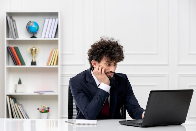 画面を見ているラップトップとオフィススーツと赤いネクタイのカスタマーサービス巻き毛のブルネットの若い男