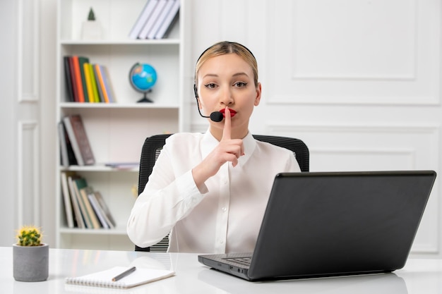 Customer service cute beautiful girl in white shirt with computer and headset showing silence sign