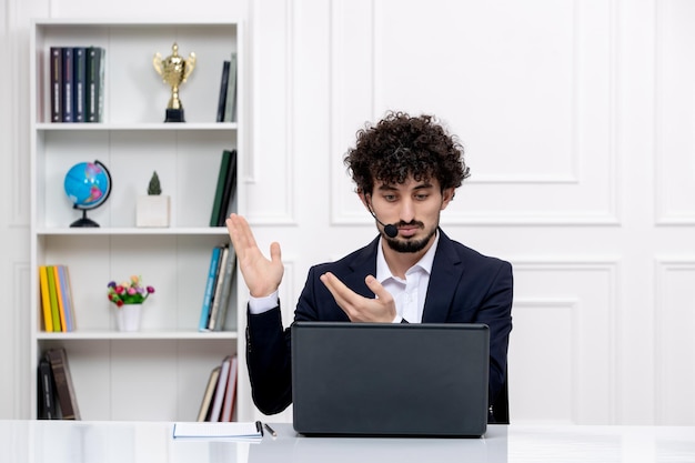 Customer service cute brunette guy in office suit with laptop and headset waving hands