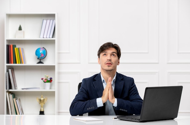 Customer service the cute brunette guy in the suit with laptop praying and looking up