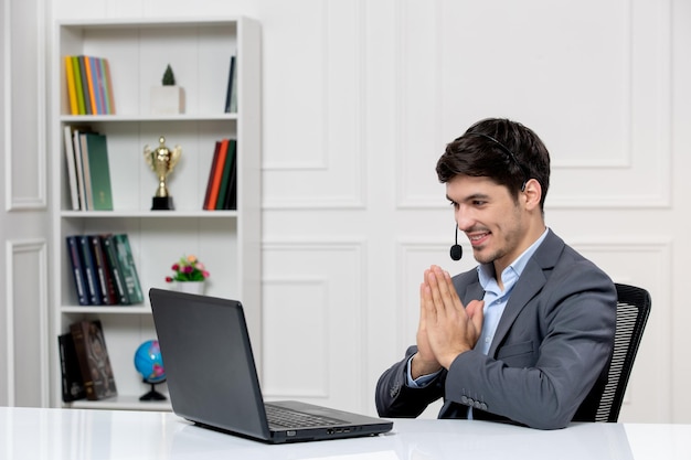 Customer service cute guy in grey suit with computer and headset saying thank you and smiling